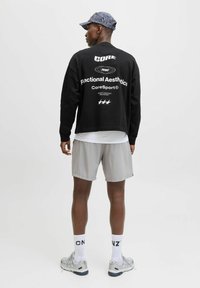 Hanorac negru cu text alb pe spate, pantaloni scurți gri deschis, șosete albe cu litere negre și încălțăminte sport gri. Căciulă cu model.
