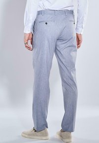 Helle graue Anzughose aus strukturierter Stoff. Sie verfügt über eine taillierte Passform, hintere Taschen mit Knopfverschlüssen und einen Bügelfalte vorne.