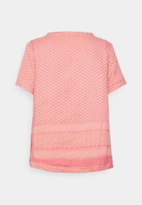 Top rosa de manga curta com uma textura estampada de desenhos geométricos e uma faixa de chevron contrastante na barra.