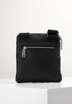 Sac bandoulière en cuir noir texturé avec poche zippée devant et sangle réglable, exposé sur un socle blanc sur un fond uni.