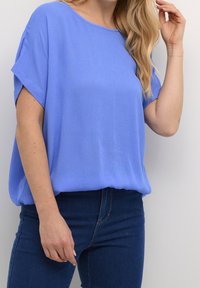 Blå bluse med korte ærmer i letvægtsstof med en afslappet pasform, der har rund halsudskæring og opsmøgede ærmer, stylet med mørke jeans.