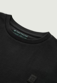 Camiseta negra de corte oversize con cuello redondo, pequeño parche de logotipo en relieve en el pecho y etiqueta "Tom Tailor" en el interior del cuello.