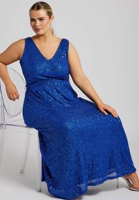 Blå paljettklänning för kvällsevenemang med V-halsringning och ärmlös design. Har en flödande kjol och en åtsittande midja för form.