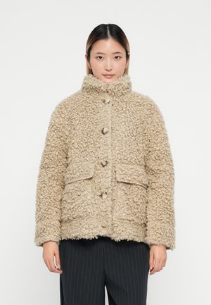 Giacca in pelliccia sintetica beige con colletto alto, caratterizzata da grandi bottoni e due tasche frontali. Materiale texturizzato dall'aspetto accogliente.