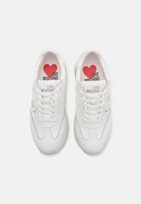 White sneakers with a smooth leather upper, round toe, and padded tongue. Features red heart logo and "LOVE MOSCHINO" branding on insoles.