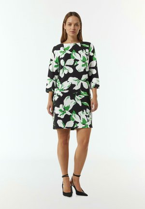 Bloemjurk met driekwartmouwen. Zwarte achtergrond met grote witte bloemen en groene accenten. Kniehoogte. Gladde stofstructuur.