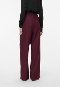 Pantaloni a gamba larga bordeaux realizzati in tessuto morbido. Design a vita alta con una vestibilità sartoriale, dotati di passanti per la cintura e sottili tasche posteriori.