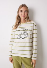 Gestreepte langemouwen shirt in crème en groen met een cartoonkatontwerp en tekst in zwart, gemaakt van zachte, lichte stof.