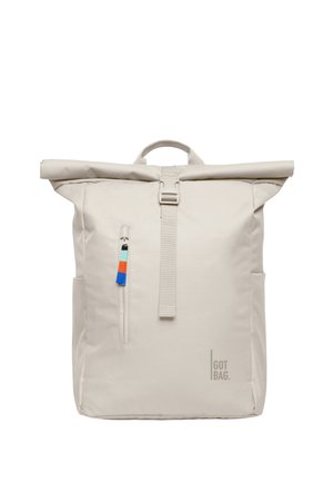 Sac à dos beige clair à rabat avec poche zippée à l'avant, muni d'une fermeture multicolore et du logo "GOT BAG" en bas à droite.