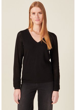 Zwarte gebreide pullover met een V-hals. Lange mouwen hebben open gebreide details. Zachte textuur met een aangesloten silhoet.