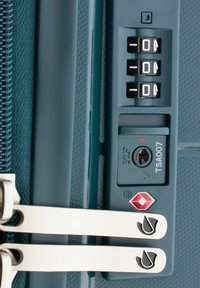 Blauwe bagagerits met een TSA-slot, cijferwieltjes die 0 tonen, zilverkleurige hardware en een getextureerd oppervlak. Geaccentueerd met een logo.