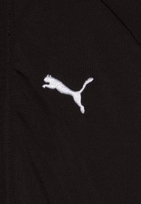 Il tessuto nero presenta un logo ricamato bianco di un puma saltante, con una texture liscia e un design semplice e atletico.