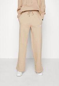 Beige cotton sweatpants with a relaxed fit, drawstring waistband, side pockets, and a small white Nike logo on the right hip.