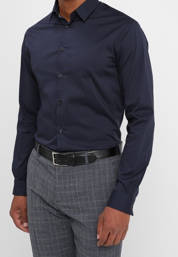 Camisa de manga larga azul marino con cierre de botones, hecha de una tela suave; combinada con pantalones de cuadros grises y un cinturón negro.