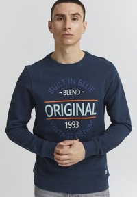 Felpa blu navy con scollatura tonda, caratterizzata da una grande stampa grafica in più colori. Materiale in misto cotone e polsini a costine.