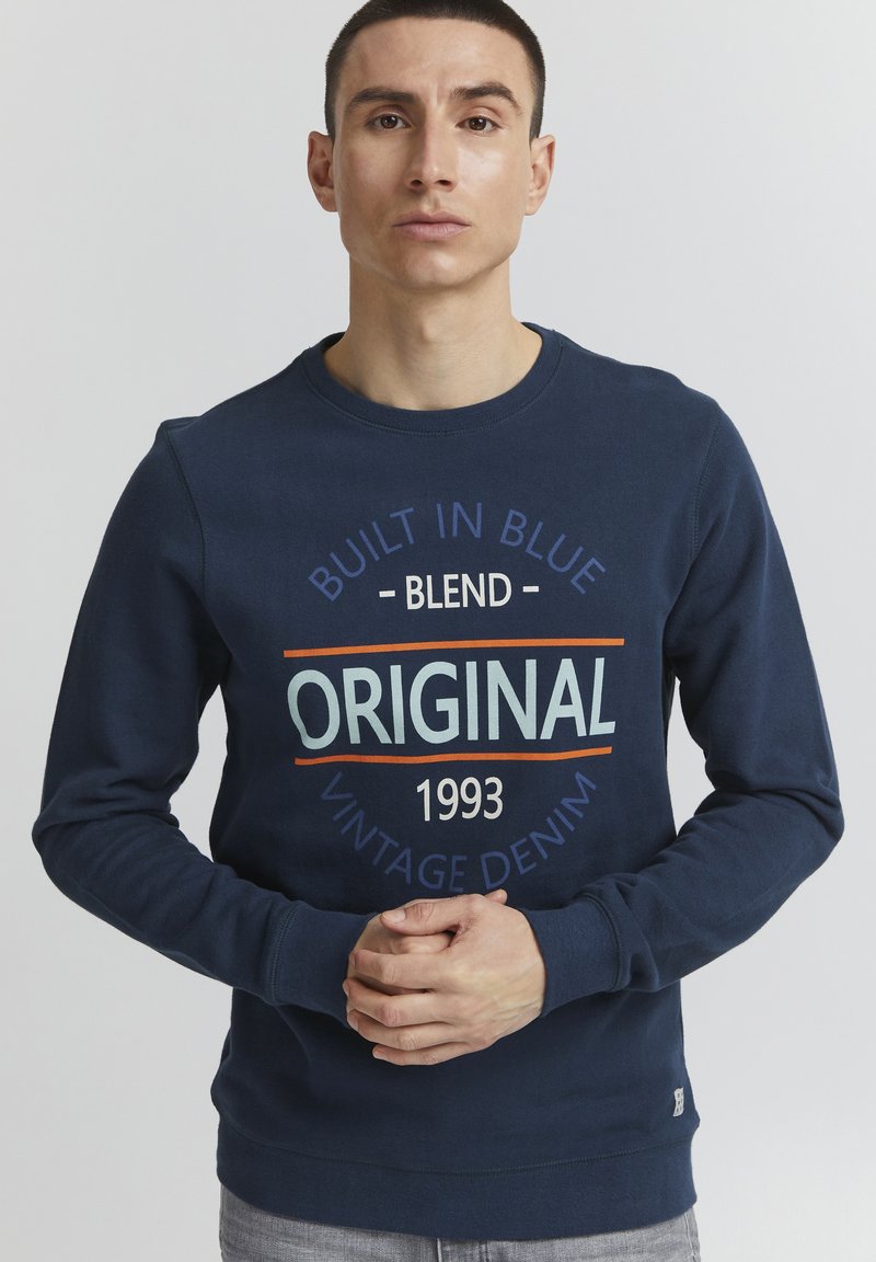Felpa blu navy con scollatura tonda, caratterizzata da una grande stampa grafica in più colori. Materiale in misto cotone e polsini a costine.