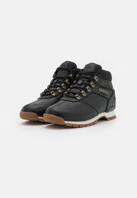 Pár černých kožených turistických bot s hnědými gumovými podrážkami, kovovými oky, polstrovaným límcem a logy Timberland na boku a jazyku.