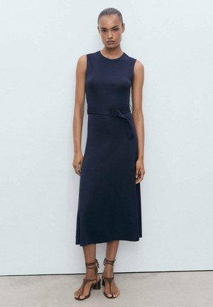 Navy sleeveless dress with a belted waist, smooth texture, and a flared hem. Paired with brown strappy heels.