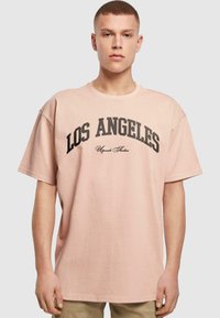 Rosa t-skjorte med korte ermer og rund hals, med "LOS ANGELES" i fete svarte bokstaver over fronten. Myk bomullstekstur.