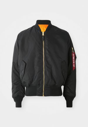 Veste bomber noire avec fermeture éclair dorée, poignets côtelés et doublure orange. Elle présente une poche latérale et une étiquette rouge de marque sur la manche.