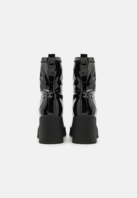 Botas de tobillo de charol negro con tacones gruesos y texturizados, que cuentan con un acabado suave y un detalle de cremallera en la parte trasera.
