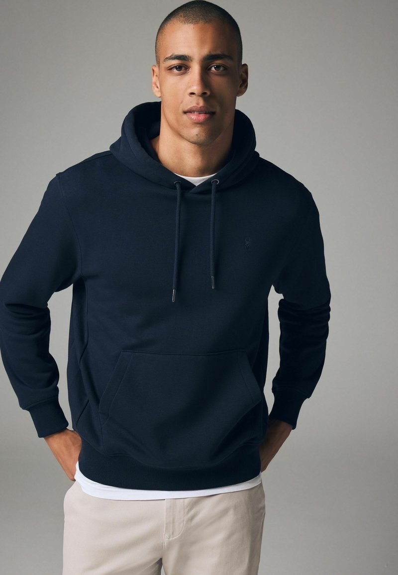 Sudadera azul marino hecha de material de sudadera, con un bolsillo tipo canguro, capucha con cordones, y puños y dobladillo de canalé. Logo sutil en el pecho.