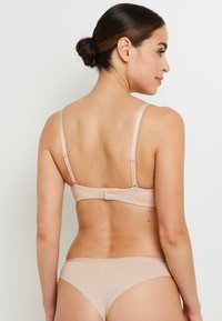 Reggiseno in nylon beige con slip coordinato. Il reggiseno ha spalline regolabili, chiusura sul retro e una texture liscia. Lo slip presenta un design semplice e senza cuciture.