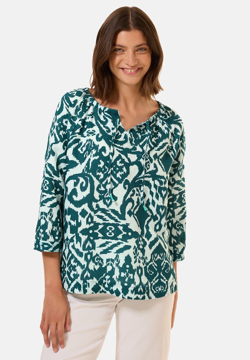 Blusa a fantasia in verde acqua e azzurro chiaro con scollo a cuore, maniche a trequarti e vestibilità comoda. Design astratti sorprendenti in tutto il capo.
