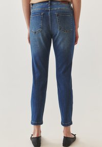 Jeans de mezclilla azul oscuro con un ajuste entallado, estilo de cinco bolsillos y puños enrollados. La tela presenta un lavado deslavado para añadir textura.