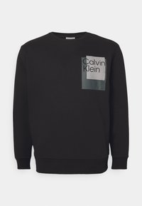 Schwarzer Pullover mit einer rechteckigen Fronttasche, die mit einer transparenten Überlagerung versehen ist, und dem Text "Calvin Klein" in fetter Schrift.
