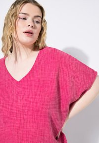 Top fucsia con scollatura a V e maniche corte, caratterizzato da un motivo a quadri testurizzato. Tessuto leggero che cade morbido attorno al corpo.