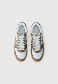 Bijele i smeđe atletske tenisice s gornjim dijelom od kože i gume, koje imaju bijele vezice, gumeni potplat i swoosh logo sa strane.