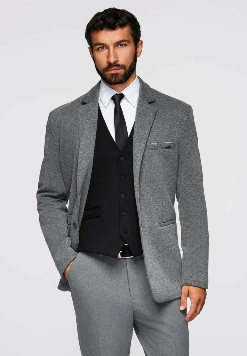 Grå kostymjacka med en slät yta, kombinerad med en svart väst, vit skjorta och svart slips. Outfitten har eleganta linjer och skräddarsydd passform.