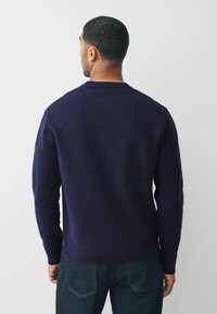 Granatowy sweter z dzianiny z okrągłym dekoltem, ściągaczami na mankietach i u dołu, z fakturowanym wykończeniem. Nosi się go na ciemnoniebieskie dżinsy.