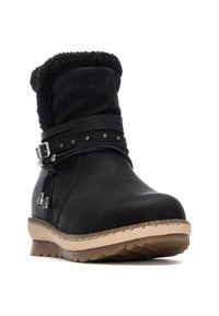 Botín negro con un suave cuello texturizado, correa con hebilla y tachuelas decorativas. Presenta una suela beige robusta con agarre texturizado.