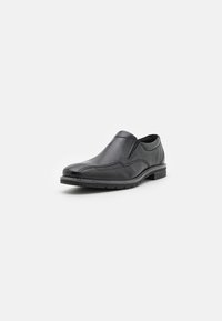 Zapato negro tipo slip-on hecho de cuero suave con costuras curvadas, punta redondeada y una suela texturizada para mayor agarre.
