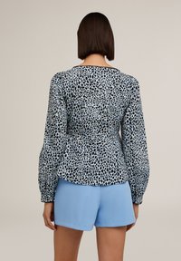 Blusa a maniche lunghe in stampa astratta nera e azzurra, con vita arricciata e maniche a sbuffo, abbinata a pantaloni corti azzurri.