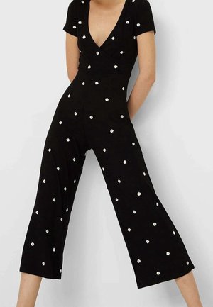 Black jumpsuit made of ribbed fabric, featuring a deep V-neck, short sleeves, and scattered white floral embroidery on the bodice and legs.