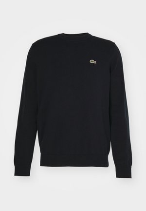 Black knit sweater with a round neckline and ribbed cuffs, featuring a small green and white crocodile logo on the left chest.