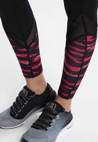 Leggings neri con un motivo a strisce tigre rosso e rosa, con accenti in rete. Abbinati a scarpe da ginnastica grigio e nere.