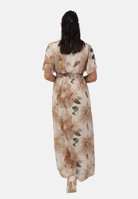 Robe maxi florale en beige clair avec de grands motifs de fleurs brunes et vertes. Présente des manches courtes et une taille élastique. Silhouette fluide.