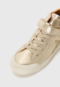 Goldfarbene metallic High-Top-Sneaker mit einem seitlichen Riemen, flachen Schnürsenkeln und strukturierten Akzenten. Gummisohle mit weißem Rand. Glatte und glänzende Oberfläche.