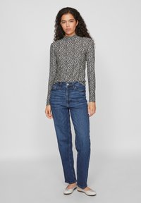 Haut à manches longues noir et blanc à motif moucheté, associé à un jean droit bleu taille haute et des chaussures plates de couleur claire.
