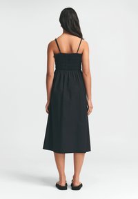 Vestido negro midi con un corsé fruncido, tirantes finos y una falda fluida. El tejido parece suave con una textura lisa. Sin patrones ni adornos.
