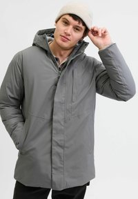 Grå isoleret parka-jakke med hætte, lynlås foran og en sidelomme. Stoffet er glat med en mat overflade.