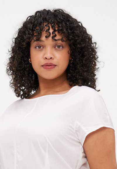 Haut blanc à manches courtes avec un col rond et des détails de couture subtils. Tissu lisse avec un léger éclat et une coupe décontractée, associé à des cheveux naturels.