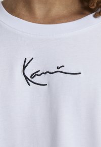 T-shirt blanc en coton avec un design de signature noir brodé. Le tissu est doux avec un col rond classique.