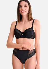Ensemble de lingerie noire comprenant un soutien-gorge balconnet avec détails en dentelle et bretelles festonnées, accompagné d'un slip taille haute avec panneaux transparents.