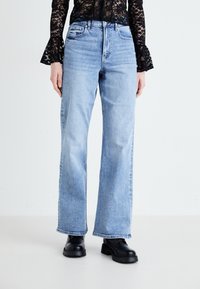 Ανοιχτό μπλε τζιν με εκρηκτική γραμμή, κατασκευασμένο από denim με ξεθωριασμένη εμφάνιση, διαθέτει πέντε τσέπες και φερμουάρ, συνδυασμένο με μαύρες πλατφόρμες μπούτς.