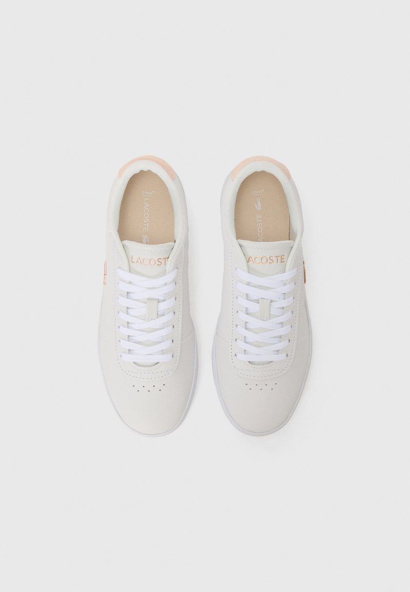 Baskets blanches avec une tige en cuir lisse, un bout rond, des lacets blancs et des accents pêche clair au niveau du talon et du logo. Design perforé simple.